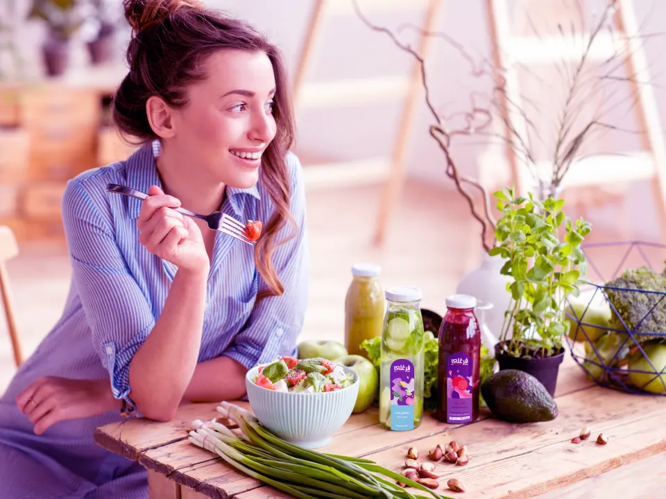 A smiling woman enjoying a fresh salad with Farghali juices on the table